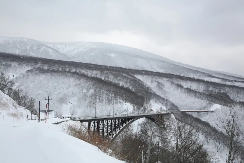 八甲田城ヶ倉大橋橫跨雪白溪谷，橋下溪流與樹冰