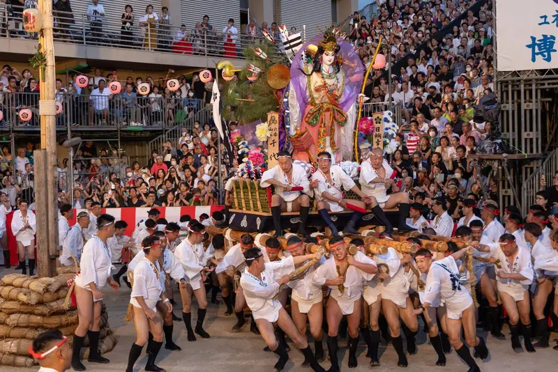 博多祇園山笠祭典中，男子扛著華麗的舁き山笠衝過博多街道
