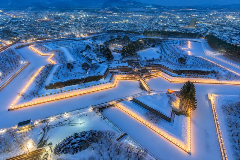 空拍視角的五稜郭，星形城郭在雪中被燈飾勾勒成發光的五芒星