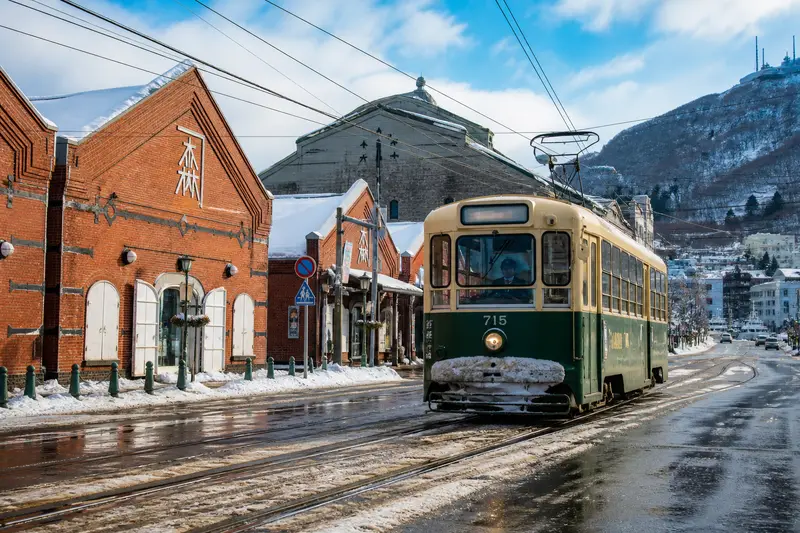 函館的復古路面電車（市電）行駛過雪後街道，背景是港町建築