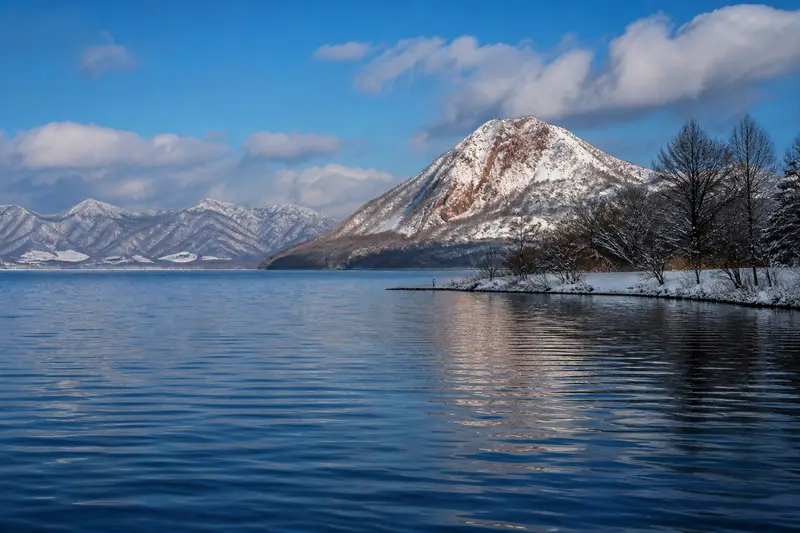 洞爺湖冬季湖景，湖面不結冰，遠處昭和新山紅褐山體覆上白雪