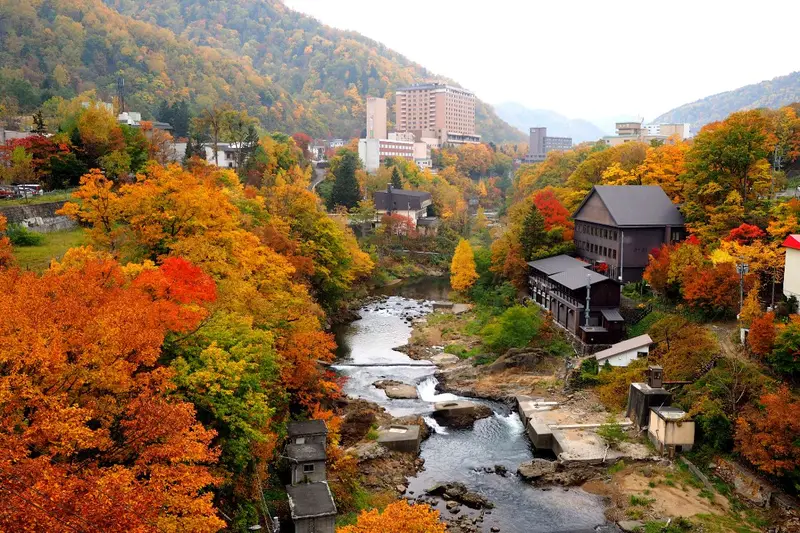 通往定山溪的山區道路，兩旁紅葉夾道，遠處是溪谷與溫泉街