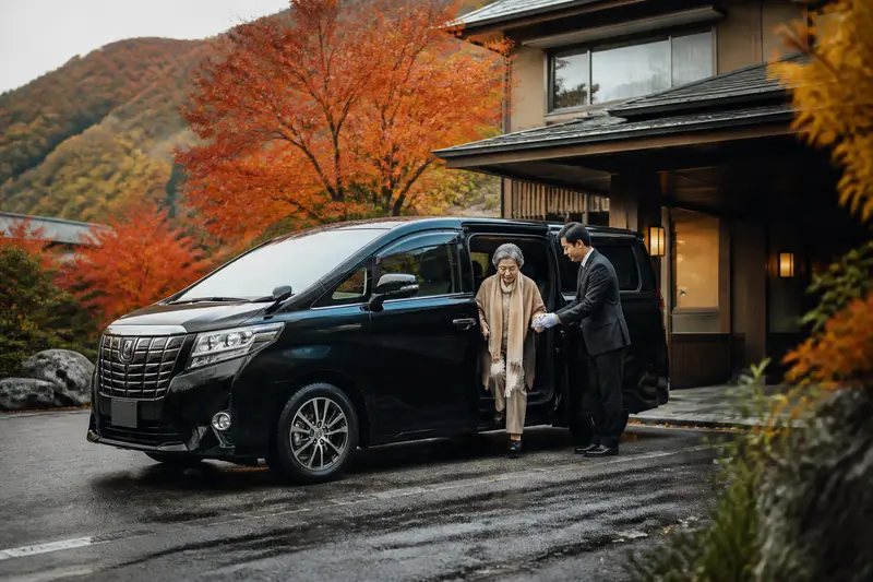 秋日定山溪的專車，中文司機協助長輩下車，背景是紅葉溪谷與吊橋