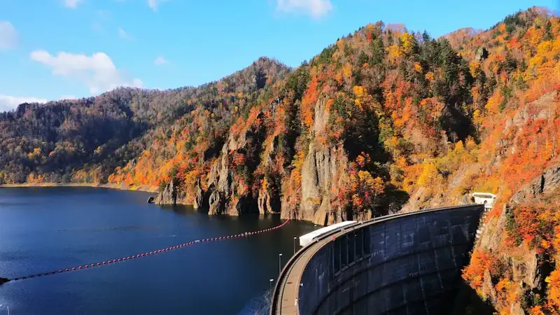豐平峽水庫的紅葉，湖面倒映整片楓紅，遠處水壩與山巒層層疊翠