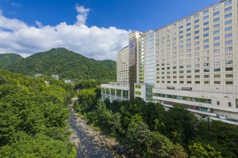 定山溪溫泉旅館的溪谷露天風呂，泡湯者眺望窗外紅葉與溪流