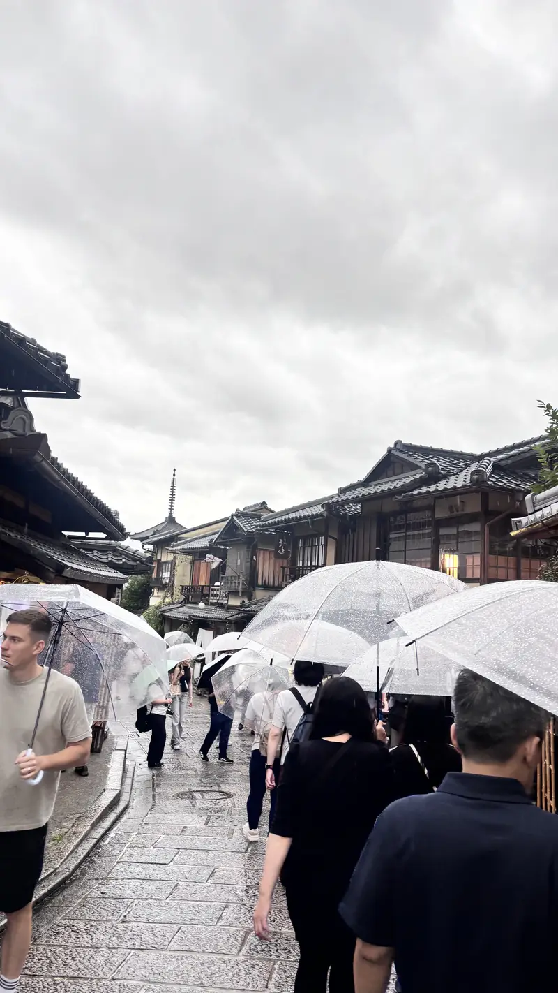 下雨天旅客撐傘在京都街頭快速拍照留念的畫面