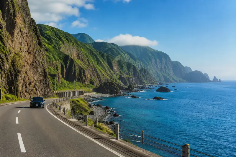 積丹海岸公路，一側是斷崖與積丹藍海，車輛沿海岸線行駛